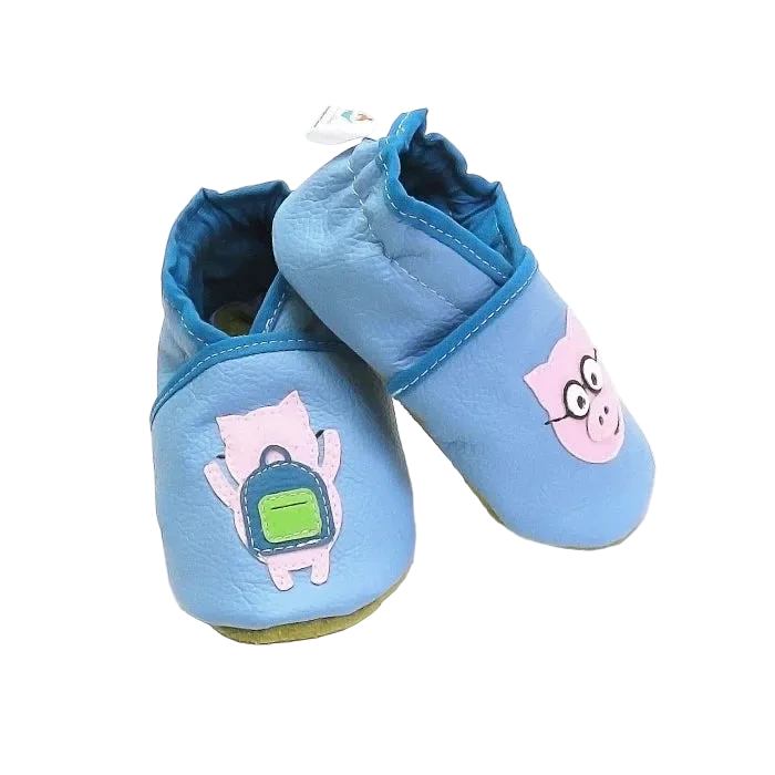 Chaussons bébé en cuir souple bleu motif cochon lunettes et cochon sac à dos, vue croisée mettant en valeur les appliqués et la texture du cuir.