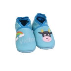 Chaussons en cuir souple artisanaux bleu clair pour bébé avec prénom brodé et motif vache noire et blanche.