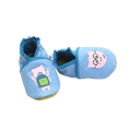 Chaussons en cuir souple artisanaux bleu pour bébé avec cochon rose à lunettes sur un pied et cochon avec sac à dos vert sur l’autre, finitions bleu foncé.