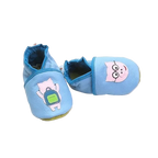 Chaussons en cuir souple artisanaux bleu pour bébé avec cochon rose à lunettes sur un pied et cochon avec sac à dos vert sur l’autre, finitions bleu foncé.