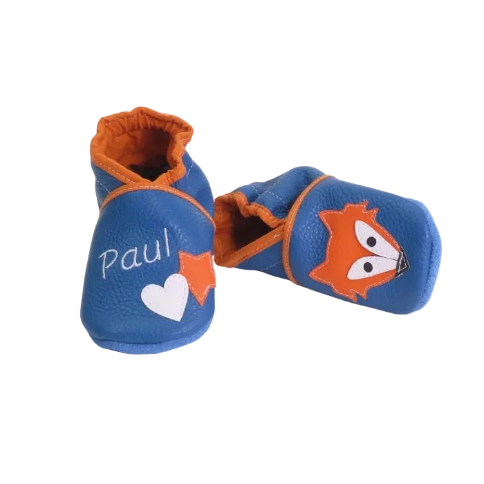 Chaussons en cuir souple artisanaux bleus pour bébé avec prénom personnalisé, renard orange sur un pied et cœur blanc sur l’autre.