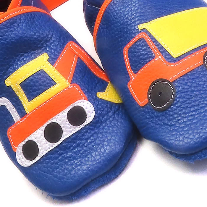 Chaussons en cuir souple artisanaux bleus pour enfant avec pelleteuse et camion benne colorés, gros plan sur les motifs.