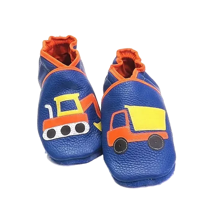 Chaussons en cuir souple artisanaux bleus pour enfant avec pelleteuse sur un pied et camion benne sur l’autre, finitions orange.