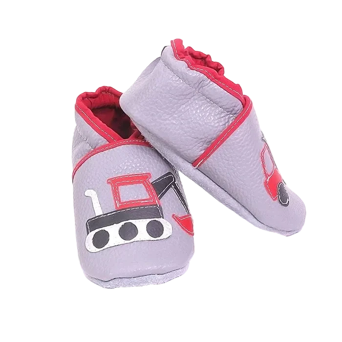 Chaussons en cuir souple artisanaux gris clair pour enfant, vue en angle, avec motifs engins de chantier rouges et noirs.