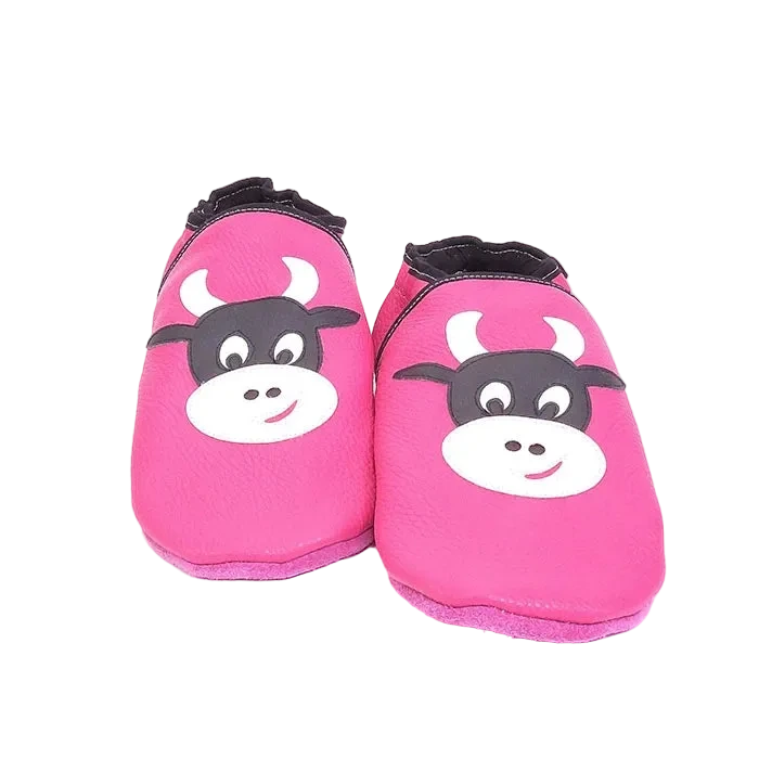 Chaussons en cuir souple artisanaux roses pour enfant avec tête de vache noire et blanche, finition élastiquée noire.