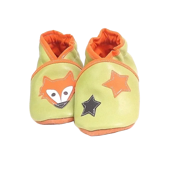 Chaussons en cuir souple artisanaux vert clair pour bébé avec tête de renard orange sur un pied et étoiles orange et noire sur l’autre.