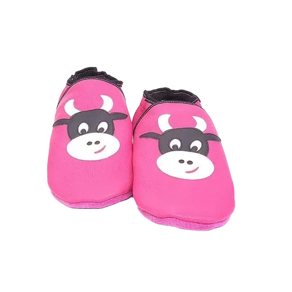 Chaussons en cuir souple artisanaux roses pour enfant, vue de face, avec motif tête de vache noire et blanche et finitions noires.