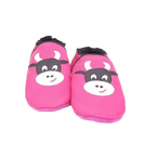 Chaussons en cuir souple artisanaux roses pour enfant, vue de face, avec motif tête de vache noire et blanche et finitions noires.