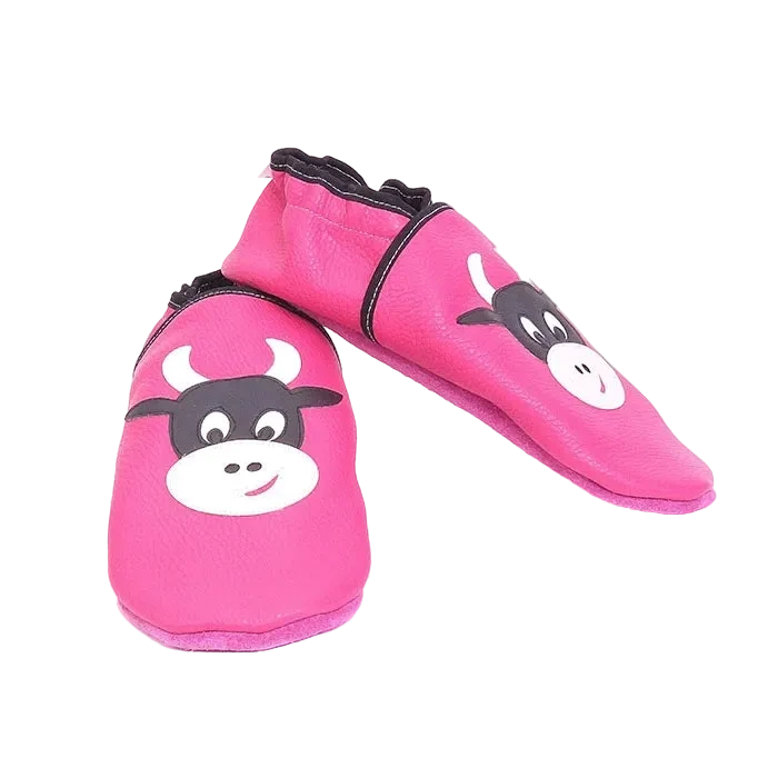 Chaussons en cuir souple artisanaux roses pour enfant, vue en angle, avec motif tête de vache noire et blanche, finitions noires.
