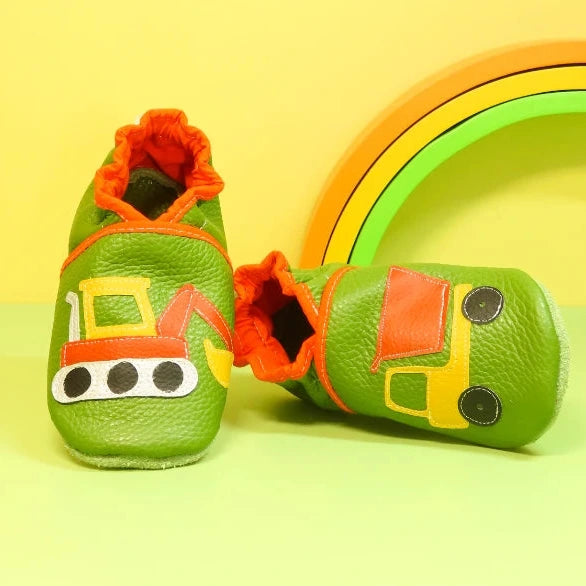 Chaussons en cuir souple artisanaux verts pour enfant, vue en angle, avec motifs pelleteuse et camion benne, détails orange et jaune.