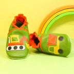 Chaussons en cuir souple artisanaux verts pour enfant, vue en angle, avec motifs pelleteuse et camion benne, détails orange et jaune.