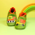 Chaussons en cuir souple artisanaux verts pour enfant, avec pelleteuse sur un pied et camion benne sur l’autre, finitions orange.