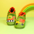 Chaussons en cuir souple artisanaux verts pour enfant, avec pelleteuse sur un pied et camion benne sur l’autre, finitions orange.