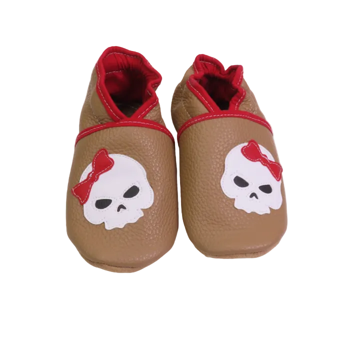 Chaussons bébé beige motif tête de mort avec nœud rouge.