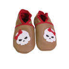 Chaussons bébé beige motif tête de mort avec nœud rouge.