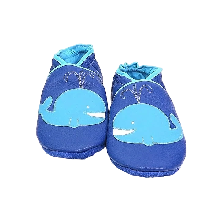 Chaussons en cuir souple artisanaux bleus pour bébé avec motif baleine bleu clair sur le dessus de chaque pied.