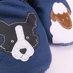 Détail des chaussons bébé en cuir souple bleu motif chien et mouton, gros plan sur les appliqués cousus et la texture du cuir.