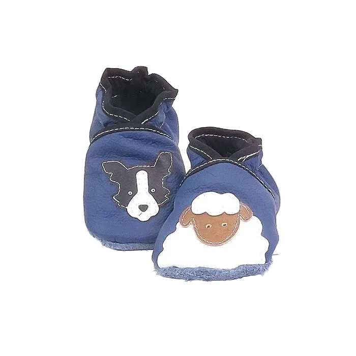 Chaussons en cuir souple artisanaux bleu pour bébé avec tête de chien noir et blanc sur un pied et mouton blanc sur l’autre, finitions noir.