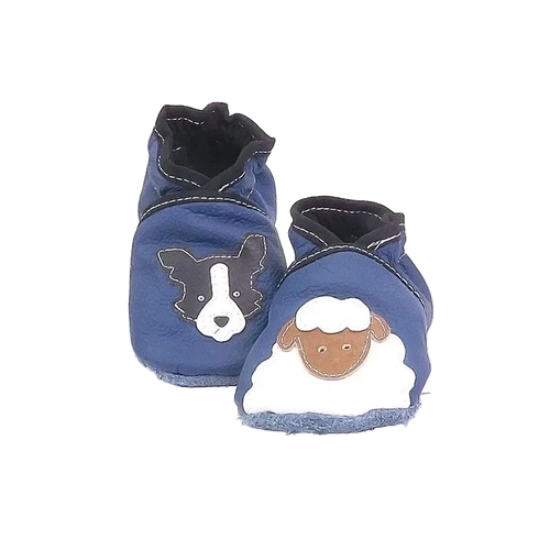 Chaussons en cuir souple artisanaux bleu pour bébé avec tête de chien noir et blanc sur un pied et mouton blanc sur l’autre, finitions noir.
