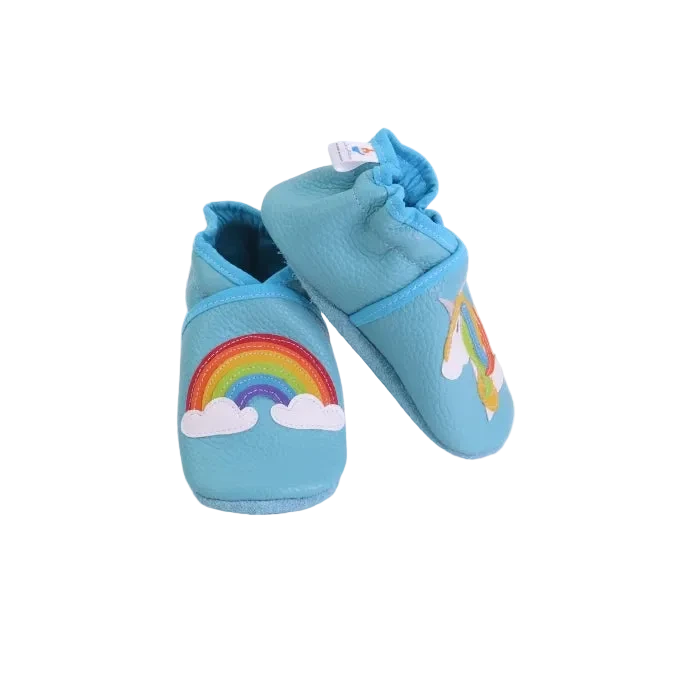 Chaussons bébé bleu ciel avec arc-en-ciel et licorne en cuir souple, vue inclinée.