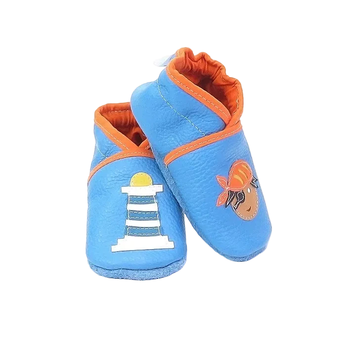 Chaussons en cuir souple artisanaux bleu clair pour bébé, vue en angle, avec pirate et phare marin cousus main.