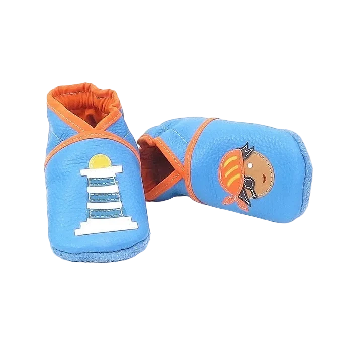 Chaussons en cuir souple artisanaux bleu clair pour bébé avec motif pirate et phare, vue avec un chausson allongé.