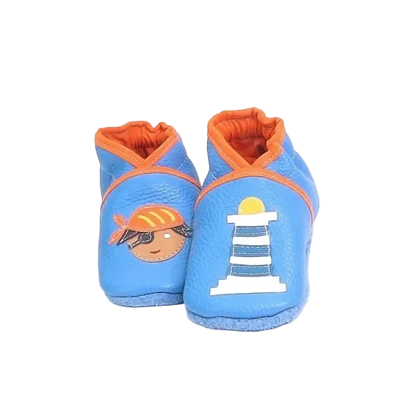 Chaussons en cuir souple artisanaux bleu clair pour bébé avec pirate illustré sur un pied et phare blanc rayé bleu sur l’autre, finitions orange.