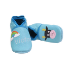 Chaussons en cuir souple artisanaux bleu clair pour bébé avec prénom brodé et motif vache noire et blanche.