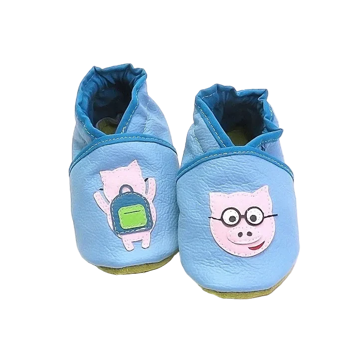 Chaussons bébé en cuir souple bleu avec cochon rose illustré et détail sac à dos, vue de face montrant les finitions contrastées.