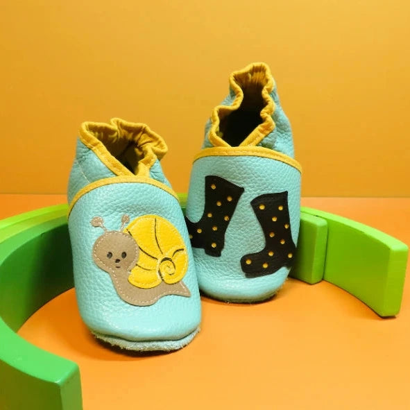 Chaussons en cuir souple pour bébé bleu ciel avec motif escargot et bottes de pluie noires à pois, vue de face.