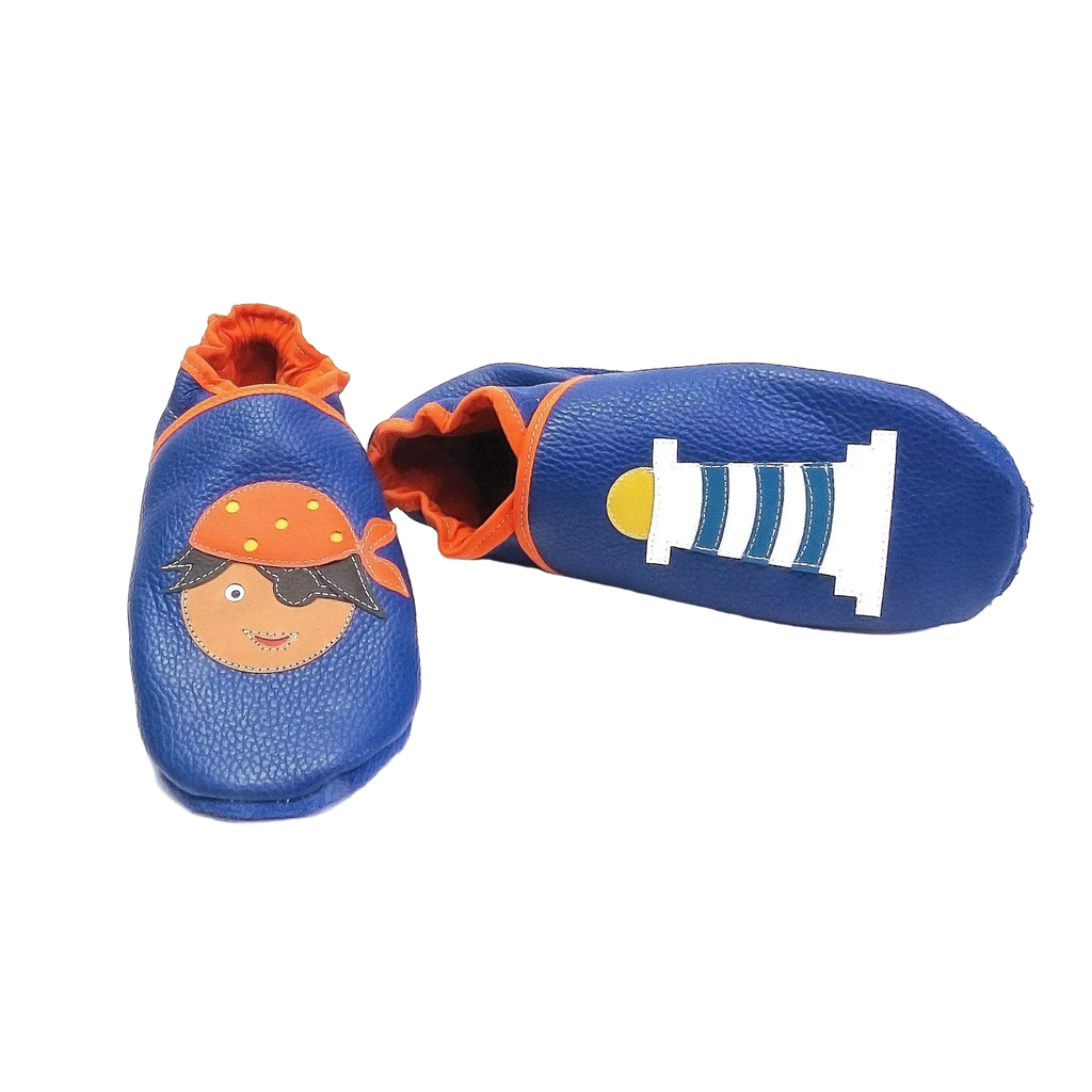Chaussons en cuir souple artisanaux bleu foncé pour bébé avec pirate sur un pied et phare blanc et bleu sur l’autre, vue avec un chausson allongé.