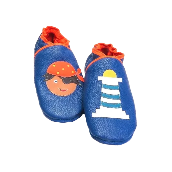 Chaussons en cuir souple artisanaux bleu foncé pour bébé avec pirate et phare blanc rayé bleu, finitions orange.