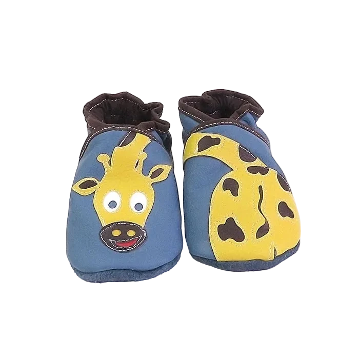 Chaussons en cuir souple artisanaux bleu pour bébé avec tête de girafe jaune sur un pied et corps tacheté sur l’autre, finitions marron.