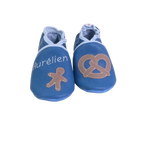 Chaussons en cuir souple artisanaux bleus pour bébé avec prénom et motifs pain d’épice et bretzel.