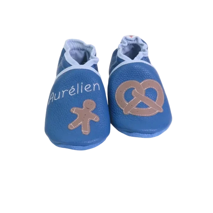 Chaussons en cuir souple artisanaux bleus pour bébé avec prénom et motifs pain d’épice et bretzel.