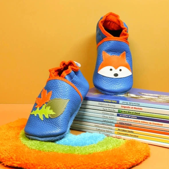 Chaussons bébé en cuir souple bleu avec renard et feuilles d’automne en mise en scène.