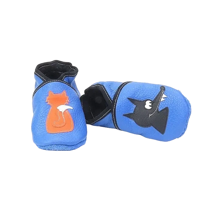 Chaussons en cuir souple artisanaux bleus pour bébé avec renard orange sur un pied et loup noir sur l’autre, vue avec un chausson allongé.