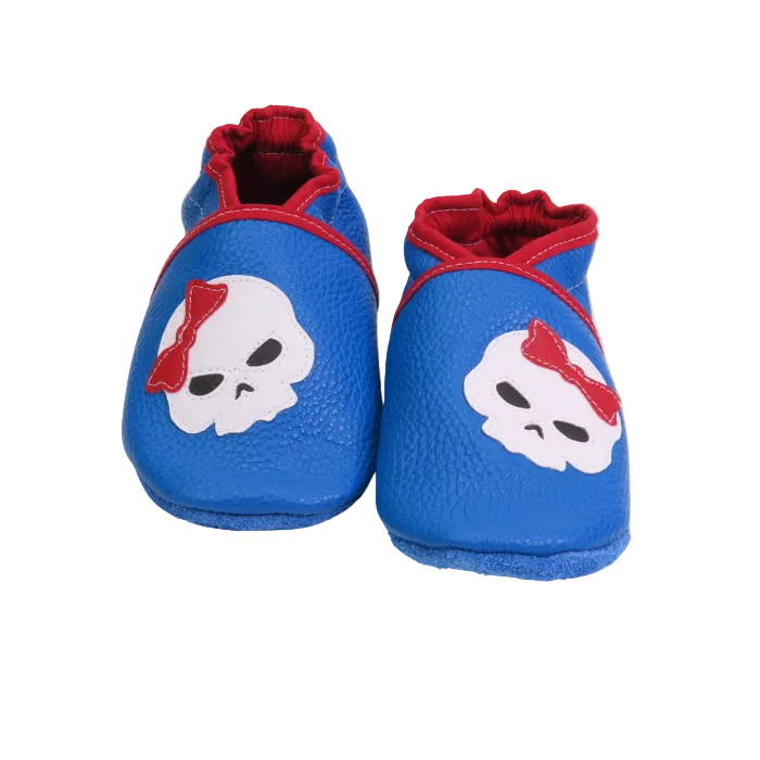 Chaussons bébé bleu avec tête de mort et nœud rouge en cuir souple.