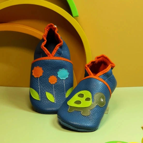 Chaussons en cuir souple pour bébé bleu avec motif tortue verte et fleurs orange et turquoise, vue de face.