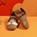 Chaussons en cuir souple cappucino pour bébé avec arc-en-ciel, nuages et étoiles décoratives, vue croisée mettant en valeur la texture du cuir.