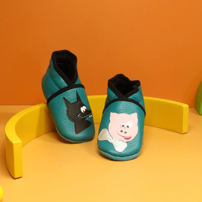 Chaussons bébé en cuir souple emeraude avec motifs loup et cochon, fabrication artisanale française.