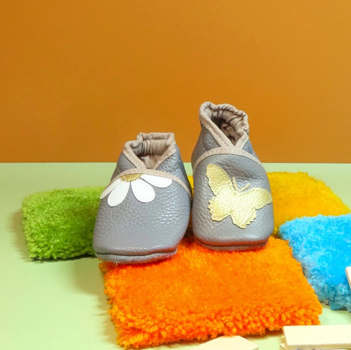 Chaussons bébé gris en cuir souple avec marguerite et papillon doré.