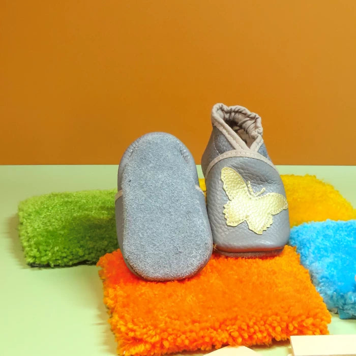 Chaussons bébé gris avec papillon doré et semelle en cuir souple.