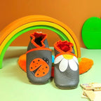 Chaussons bébé gris en cuir souple avec pâquerette blanche et coccinelle orange appliquées.