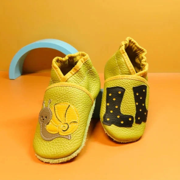 Chaussons bébé en cuir souple jaune avec escargot et bottes de pluie appliquées, fabrication artisanale française.