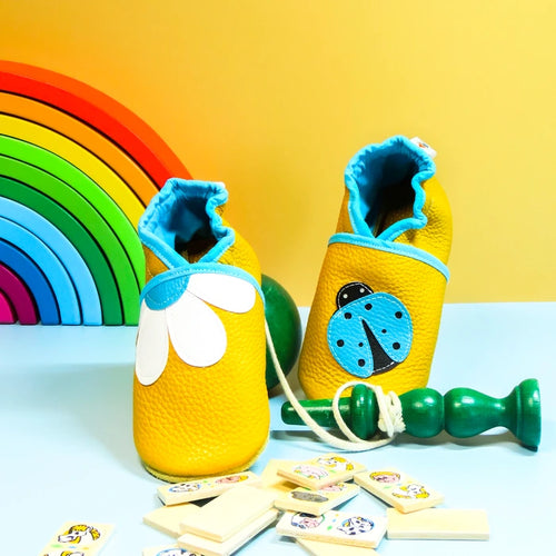 Chaussons bébé en cuir souple jaune avec pâquerette blanche et coccinelle bleue appliquées, fabrication artisanale.