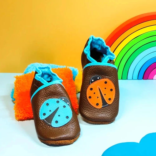 Chaussons bébé en cuir souple marron avec motif coccinelle orange et bleue appliqué sur le dessus.