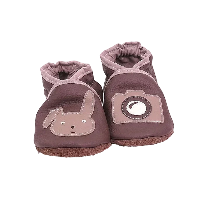 Chaussons bébé en cuir souple marron motif lapin et appareil photo, vue de face mettant en valeur les appliqués et les finitions ton sur ton.