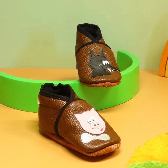 Chaussons bébé en cuir souple marron avec motifs loup et cochon, fabrication artisanale française.