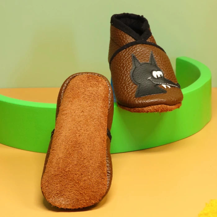 Chaussons bébé en cuir souple marron avec motif loup et semelle en cuir suédé antidérapant.